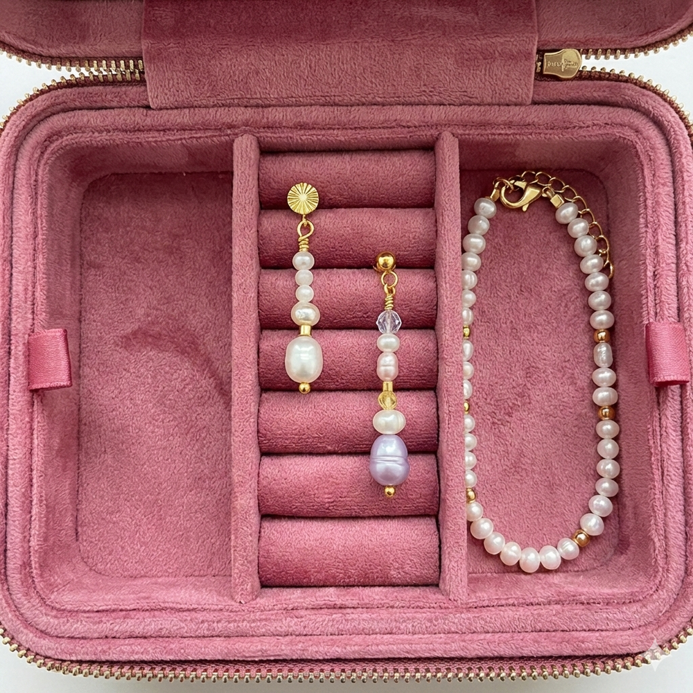 Åbent rejsesmykkeskrin i velour der viser organiseret opbevaring af øreringe og armbånd i de indvendige rum